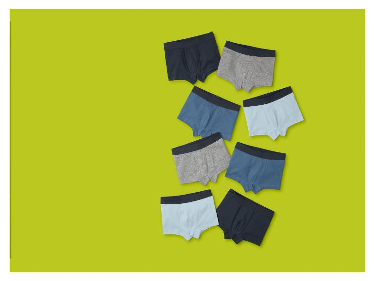 Acht jongensboxershorts in verschillende tinten blauw en grijs op een limoengroene achtergrond.