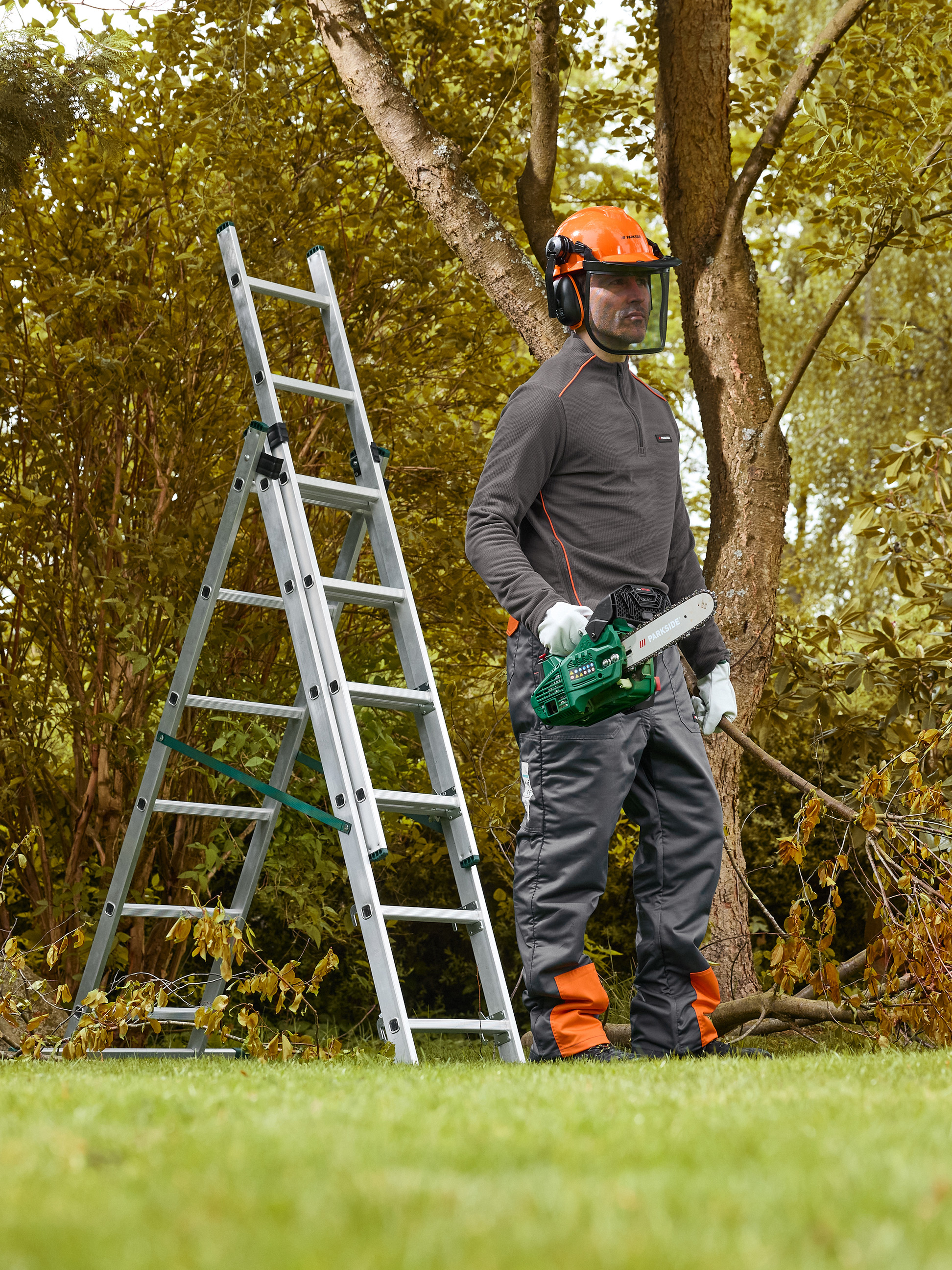 Man met veiligheidshelm en kettingzaag naast een ladder, klaar om bomen te snoeien.