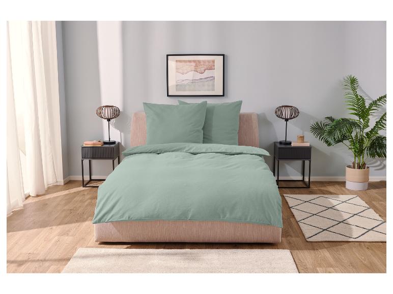 Sagegroene beddengoedset en decoratief tapijt in een moderne slaapkamer.
