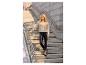 Vrouw in beige vest en zwarte imitatieleer legging op betonnen trap.