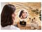 Vrouw brengt make-up aan voor een verlichte spiegel, met een telefoon die ernaast oplaadt.