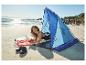 Vrouw leest boek in strandtent op zandstrand met zee op de achtergrond.