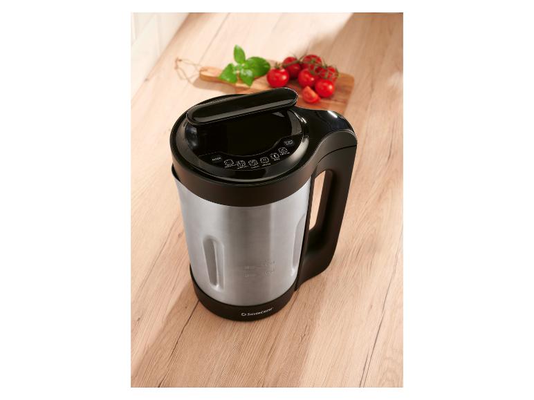 Soep- en smoothiemaker op een houten tafel, met tomaten en basilicum.