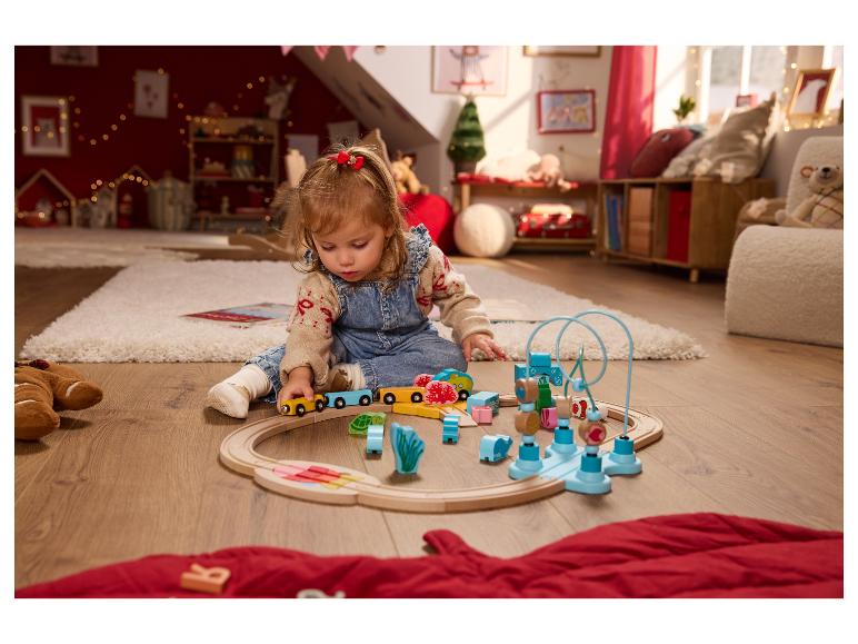 Peuter speelt met een houten speelgoedtrein en ander kleurrijk houten speelgoed op een vloerkleed.