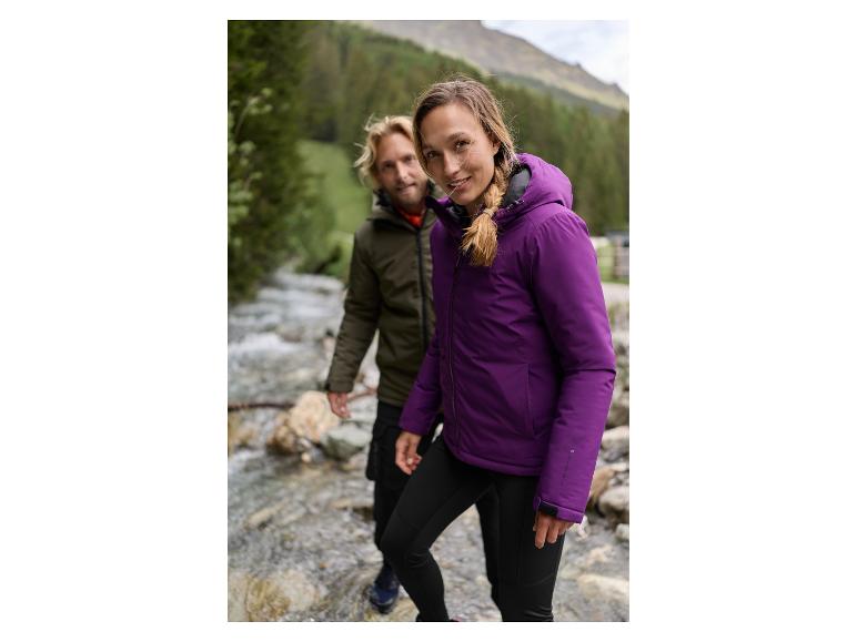 Twee mensen in outdoorjassen en -broeken, staand bij een beek in een bergachtig gebied.