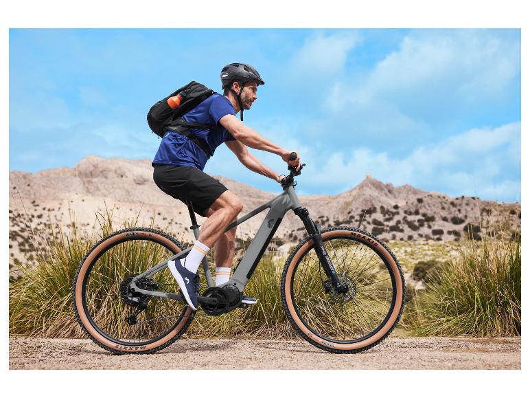 Fietser op een elektrische mountainbike met rugzak en helm in bergachtig landschap.