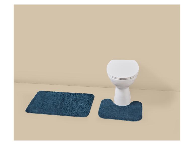 Set blauwe badmatten met toiletmat op een zandkleurige vloer.