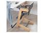 Houten en grijze kinderstoel met kom en lepel op het dienblad, naast een tafel.