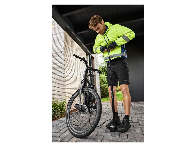 Man in neongele jas en zwarte korte broek pompt een fietsband op met een vloerpomp.