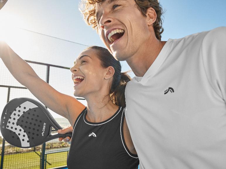 Twee blije mensen in sportkleding, één met een padelracket, op een zonnige baan.