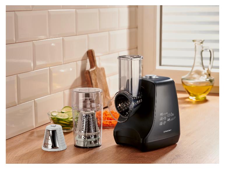 Zwarte keukenmachine met accessoires, geraspte groenten en olie in een keuken.