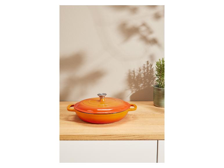 Een feloranje gietijzeren pan op een houten tafel.