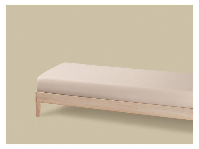 Een lichtbeige matras op een houten bed tegen een beige achtergrond.