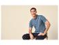 Man in blauwe poloshirt en donkere jeans, zittend en lachend.
