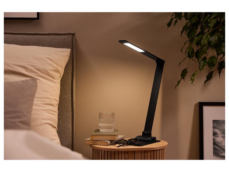 Tafellamp op een nachtkastje met boeken, een glas water en een bril naast een bed.