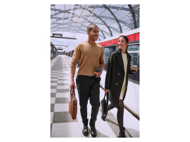 Een man en een vrouw met tassen en koffiebekers op een treinstation.