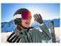 Een glimlachende vrouw met een CRIVIT skihelm en premium fotochromatische skibril op een piste.