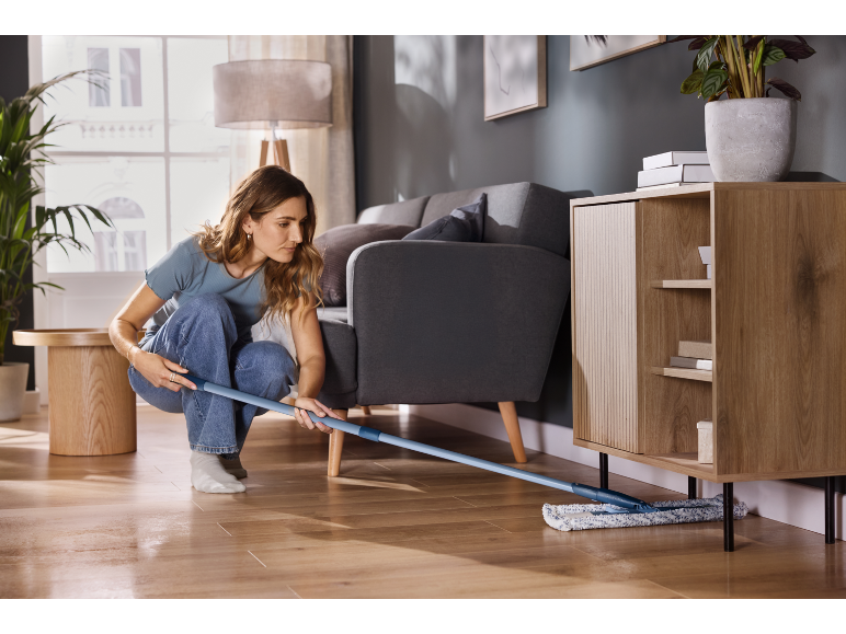 Vrouw maakt houten vloer schoon met een platte dweil in een moderne woonkamer.