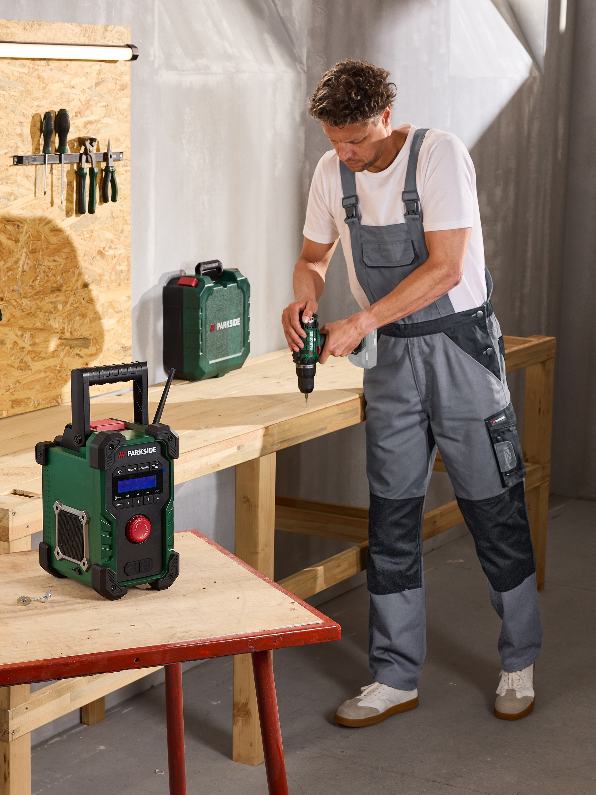 Man boort in hout, met radio en gereedschapskoffer in een werkplaats.