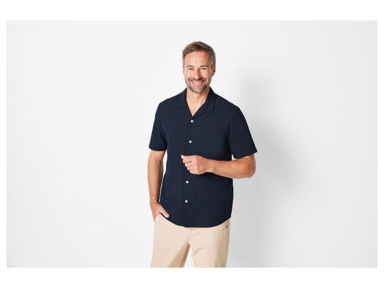 Een man in een kort mouw overhemd en beige broek.