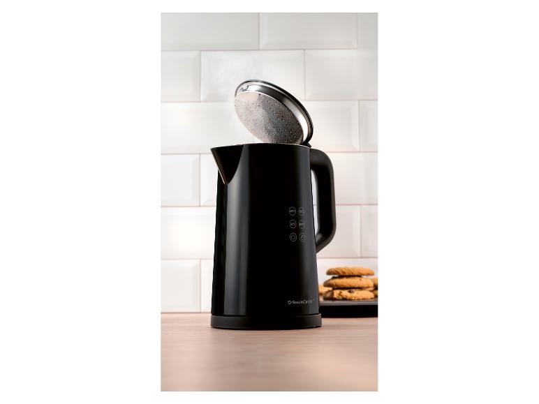 Zwarte waterkoker met open deksel en koekjes op een houten tafel.