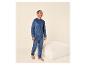 Man in blauwe velours pyjama, staand naast een beige poef.
