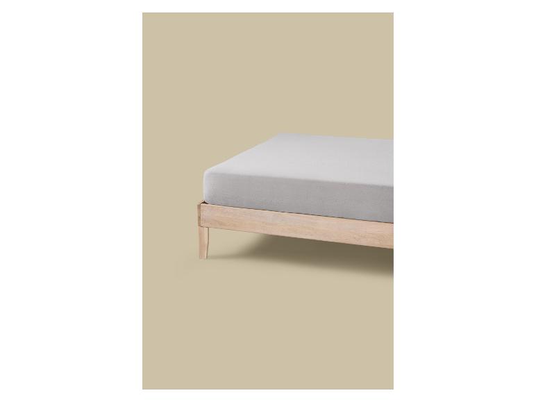 Een lichtgrijs hoeslaken op een houten bedframe tegen een beige achtergrond.