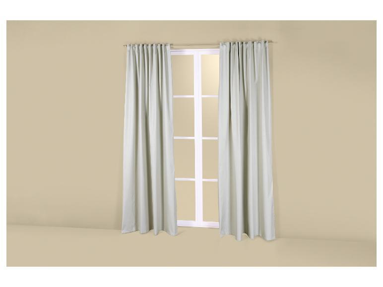 Een raam met lichtgrijze gordijnen in een kamer met beige muren.