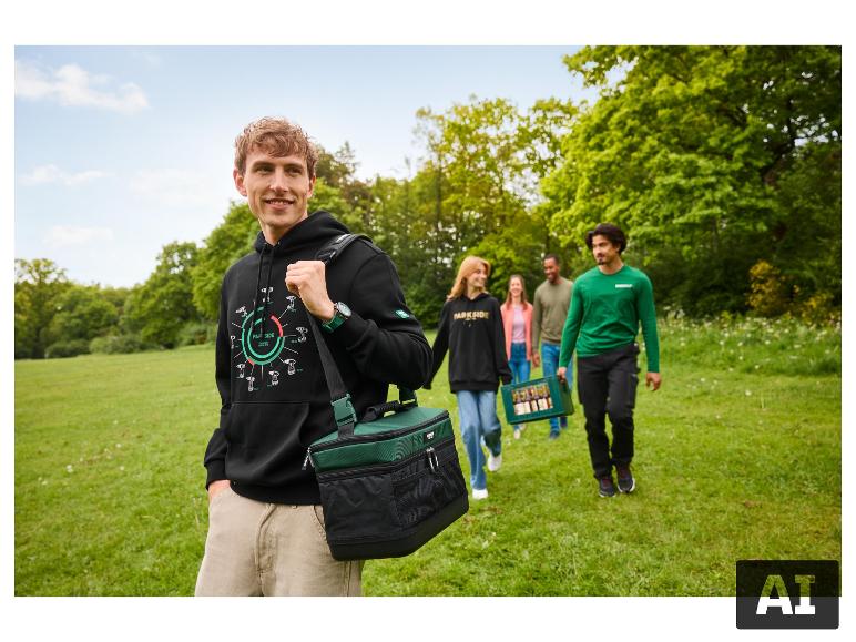 Man in zwarte hoodie met groene koeltas, wandelend met vrienden in een park.