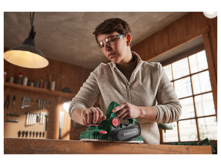 Een vrouw gebruikt een Parkside schaafmachine om hout te bewerken in haar werkplaats.