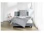 Grijs bed met geometrisch beddengoed, nachtkastje met lamp en witte gordijnen.