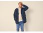 Man in donkerblauwe parka, beige trui, jeans en muts