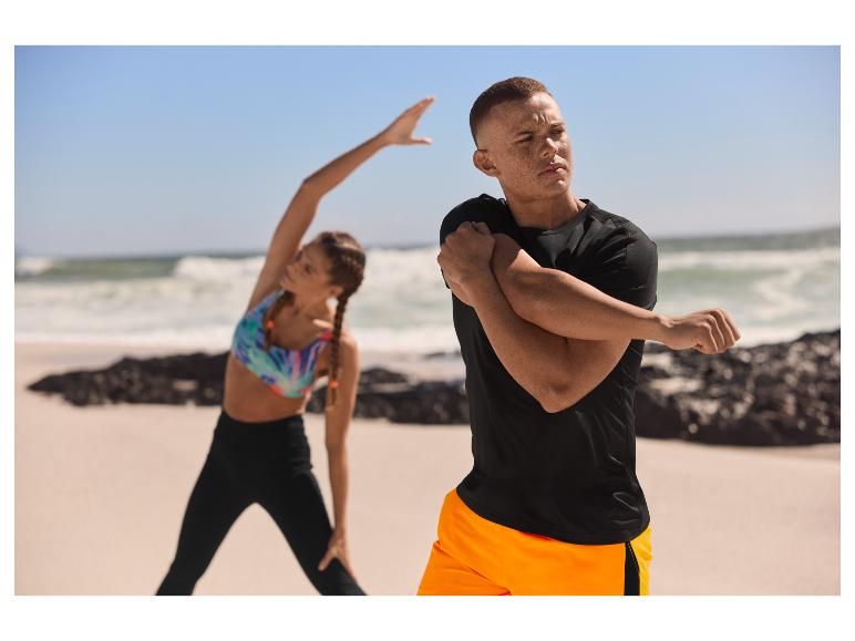 Man en vrouw rekken en strekken zich op het strand in sportkleding.