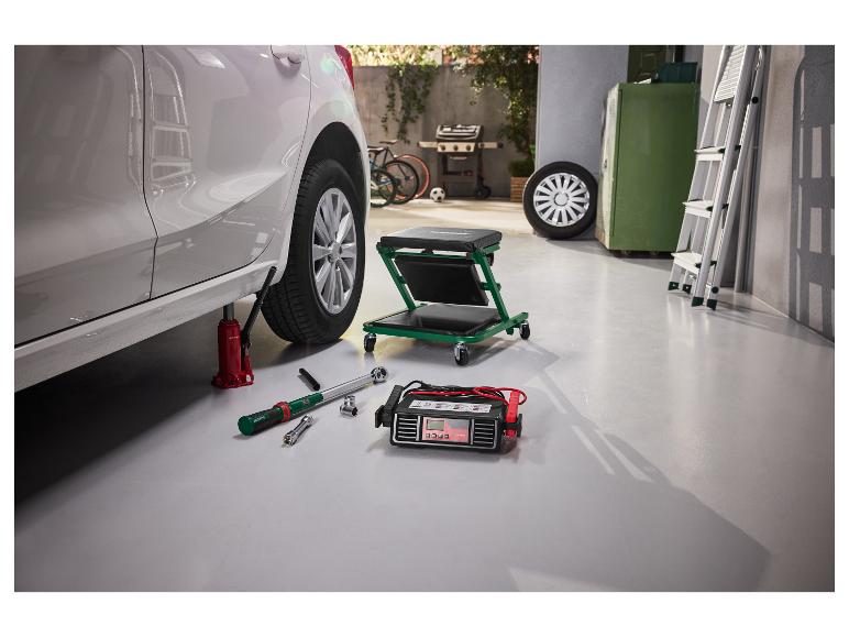 Autokrik, momentsleutel en acculader in een garage bij het verwisselen van een autoband.
