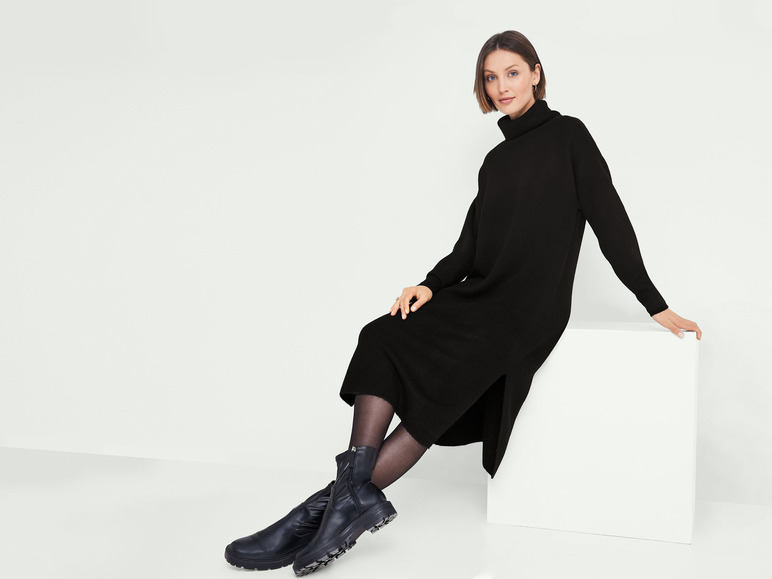 Een vrouw draagt een zwarte gebreide jurk met laarzen.