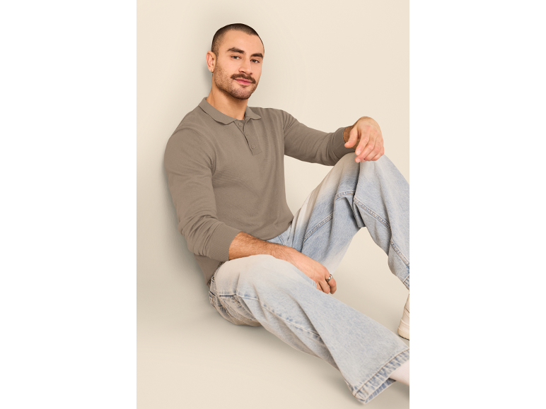 Man in een poloshirt met lange mouwen en lichtblauwe jeans, zittend op de grond.