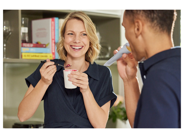 Een vrouw eet yoghurt uit een bekertje terwijl ze met een man praat.