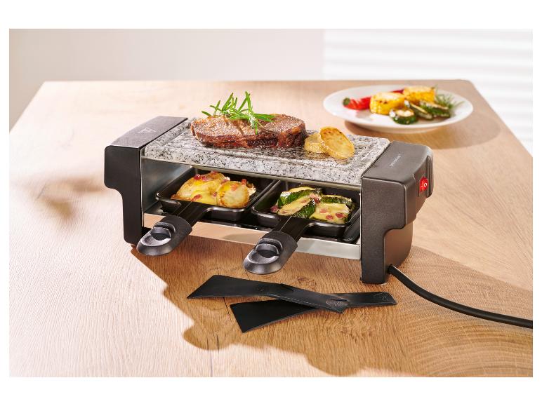 Raclette grill met biefstuk, aardappelen en courgette op een houten tafel.