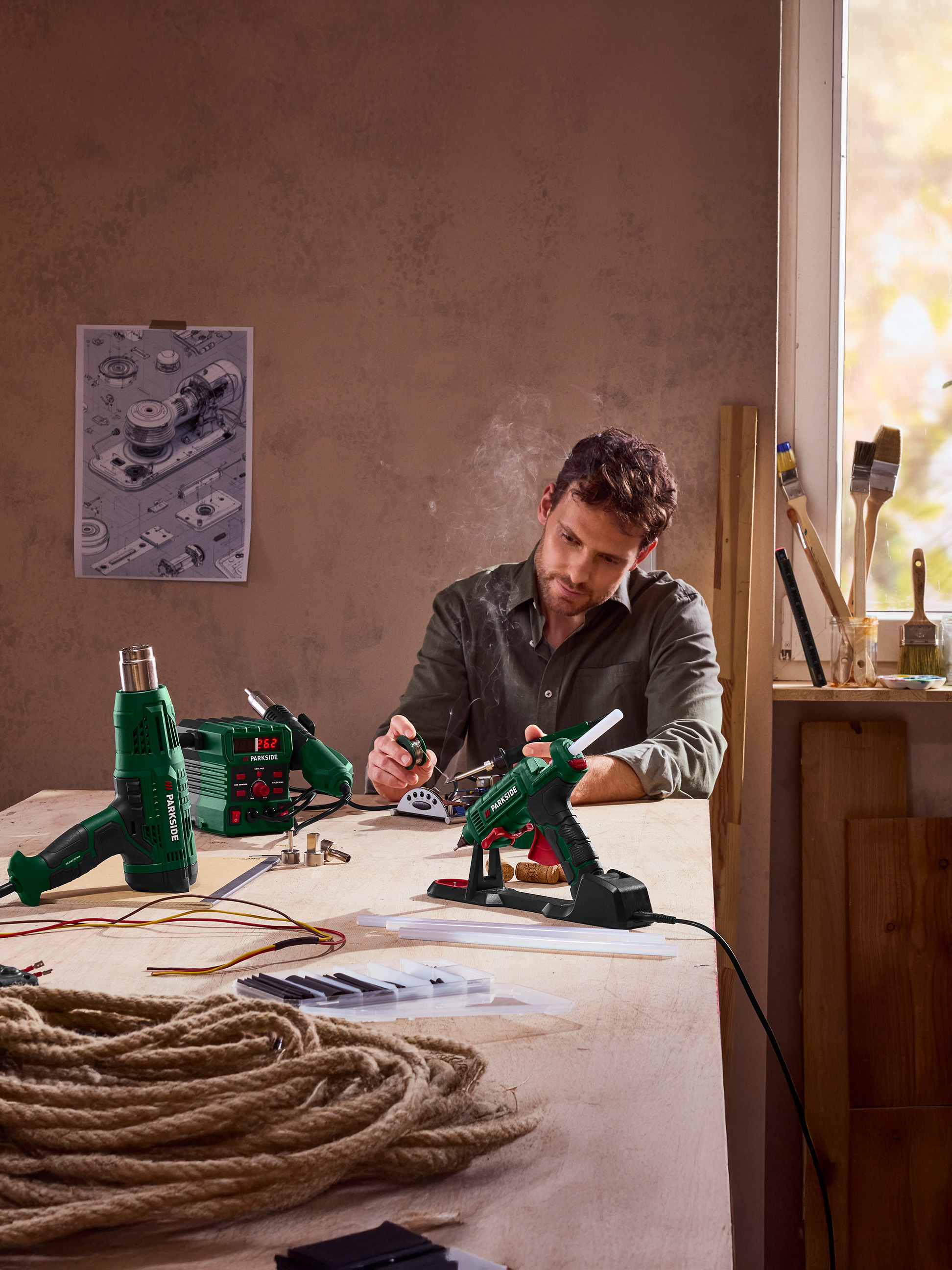 Man gebruikt een lijmpistool, met een heteluchtpistool en soldeerbout op tafel.