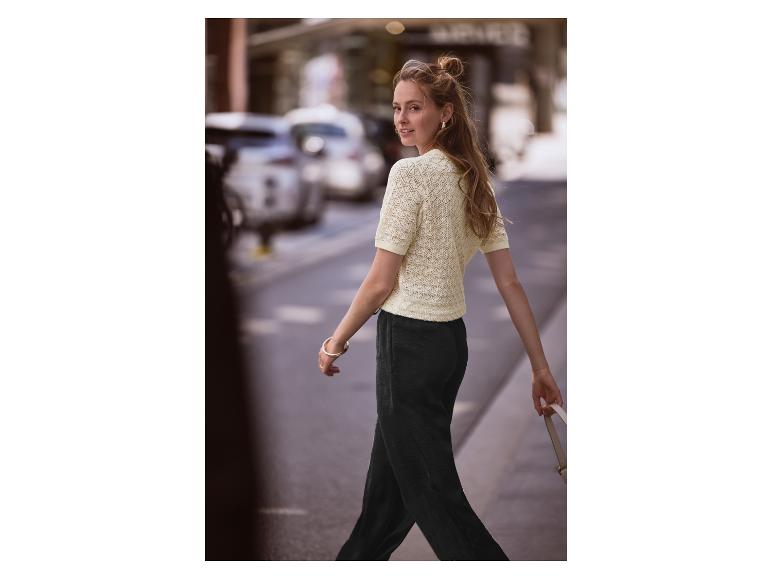 Vrouw loopt over straat met een crèmekleurig gebreid topje en een donkere broek aan.