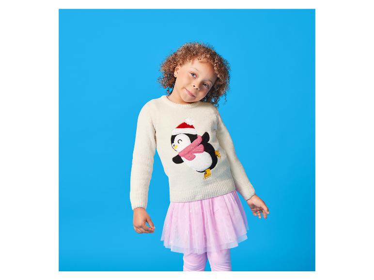 Meisje met krullend haar in een pinguïntrui en een roze tutu rok.