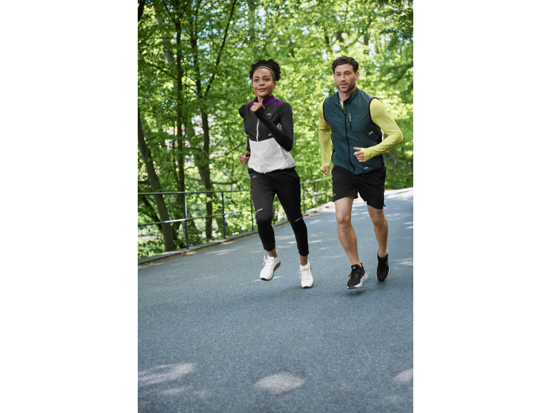 Twee hardlopers in sportkleding joggen buiten, vrouw in een jas en man in een vest.