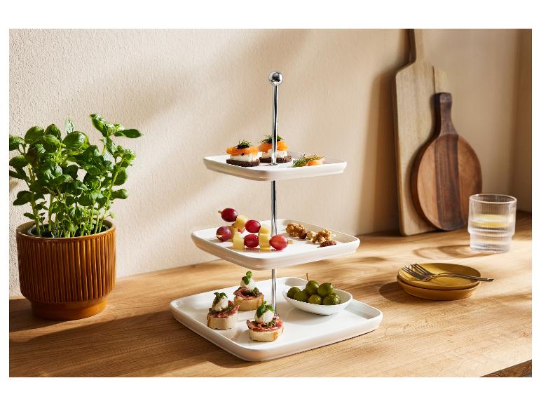 Een drielaags serveerplateau met diverse hapjes, naast een basilicumplant en keukengerei.