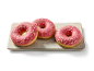 Drie roze geglazuurde donuts met sprinkles op een rechthoekig bord.