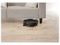 Zwarte robotstofzuiger reinigt onder een lichte bank op een houten vloer.