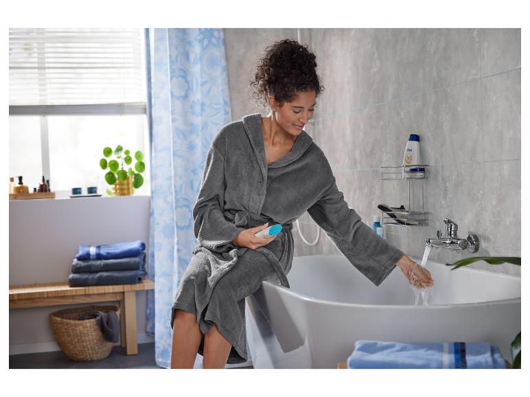 Een vrouw in een badjas vult een bad met water.