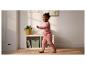 Kind in roze outfit loopt in een kamer met een rek en een plant.