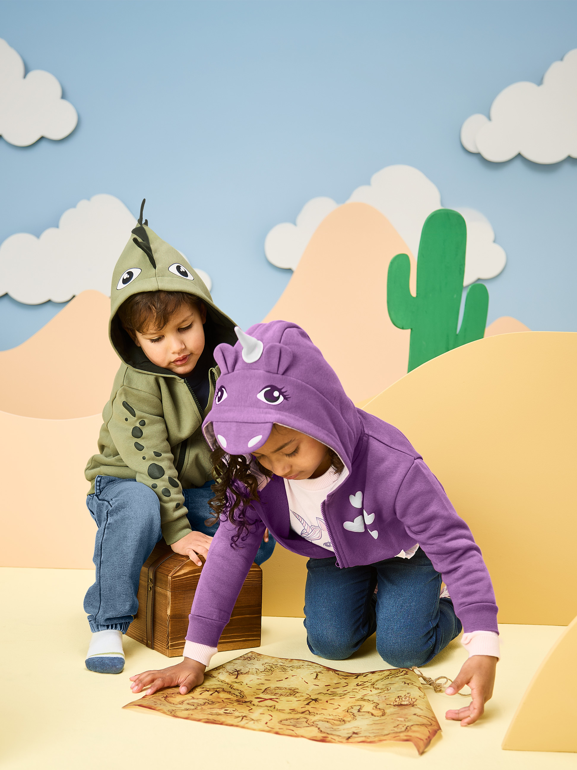 Kinderen in dinosaurus- en eenhoornhoodies, kijkend naar een schatkaart.