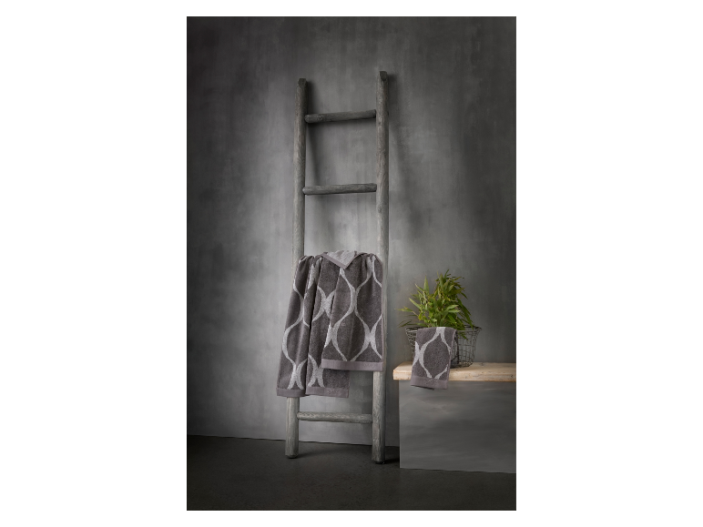 Loops & Looks badhanddoeken hangen aan een houten ladder tegen een grijze muur.