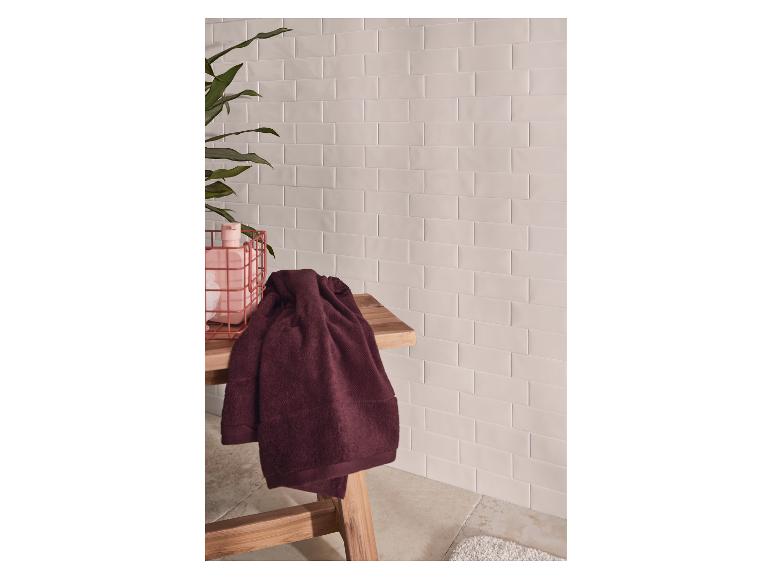 Badhanddoeken op een houten bankje, met betegelde muren en een plant.